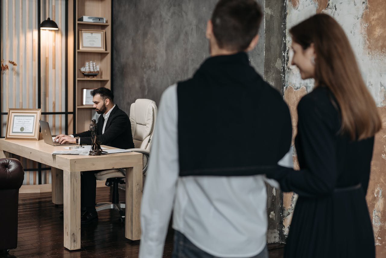mobile-02 A business consultant working at a desk while a couple in formal wear approaches him in a modern office setting.